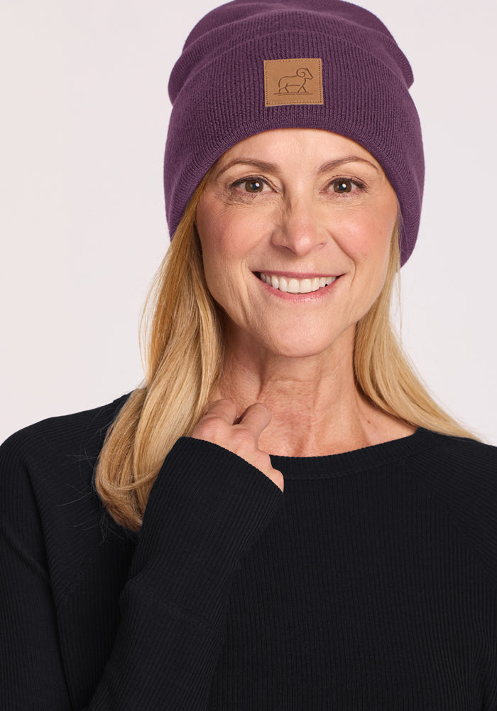 Smiling blonde woman wears the Woolx Baylor Beanie in Purple Iris and a black sweater, posing against a plain backdrop.