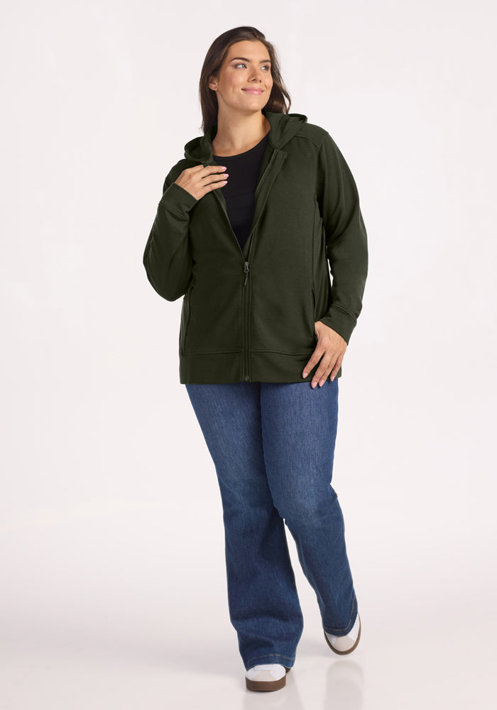 Woman in a Woolx Darby Zip Up Hoodie - Duffel Bag, black shirt, blue jeans, and white shoes smiles by a white background.
