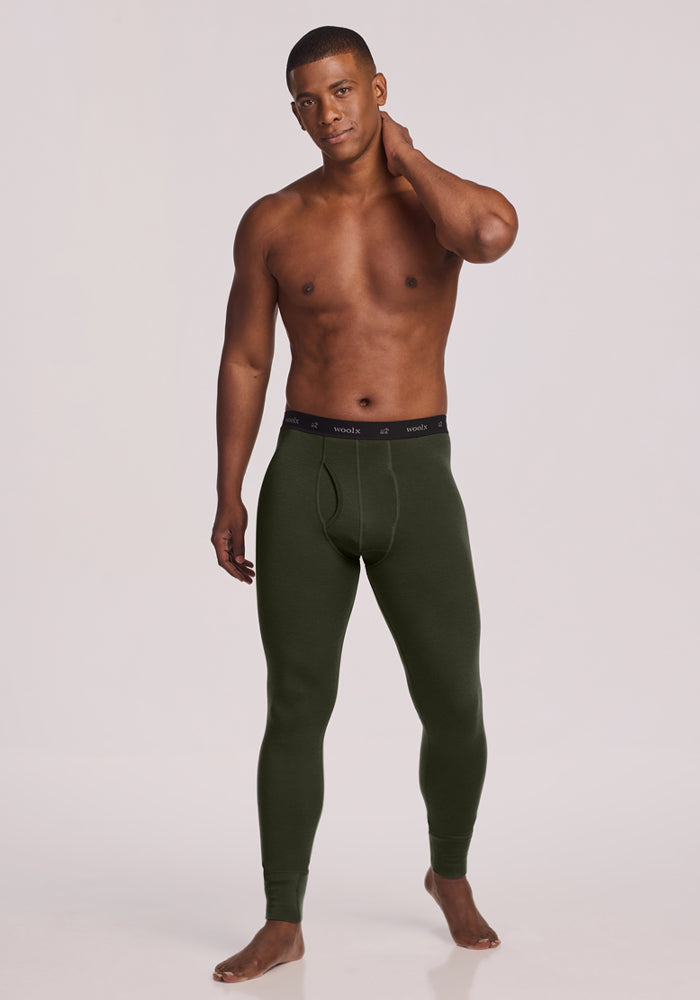 A man stands barefoot in Woolx Arctic Leggings - Duffel Bag, one hand on his neck, against a plain background.