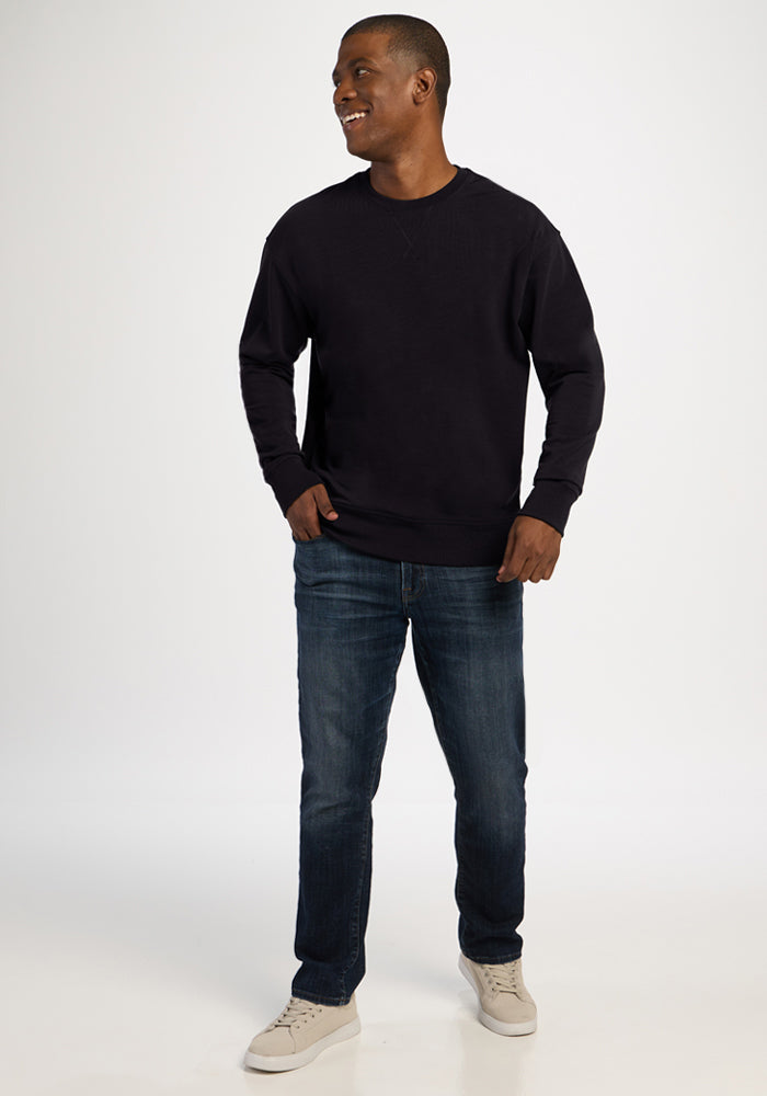 A man wearing a black Woolx Miles Crewneck sweater, blue jeans, and light-colored sneakers.