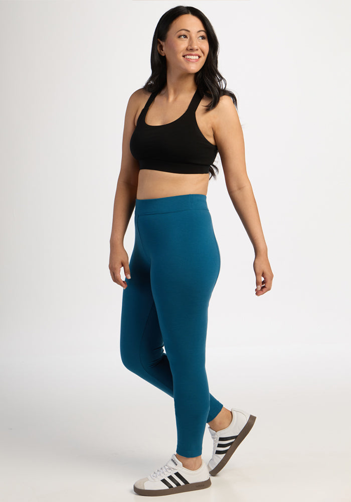 Smiling woman in Woolx Stella Leggings - Blue Pine stands against a plain white background, wearing a black sports bra.