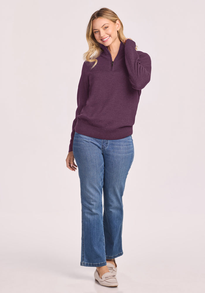 Woman in Woolx Collins Half Zip Sweater - Purple Iris and jeans touches her hair against a plain background.