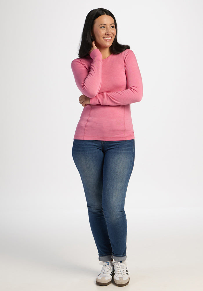 Woman smiling in a Woolx Hannah Long Sleeve Top – Pinky Promise, blue jeans, and sneakers against a white background.
