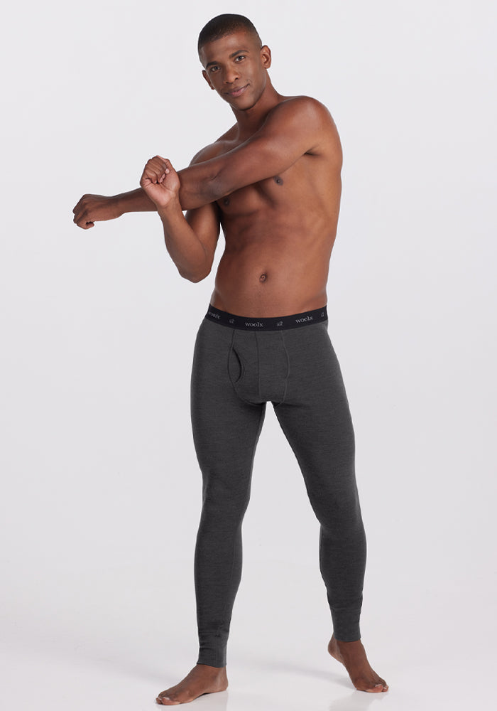 A man in Woolx Backcountry Leggings - Cinder Melange stretches his arm across his chest against a white background.