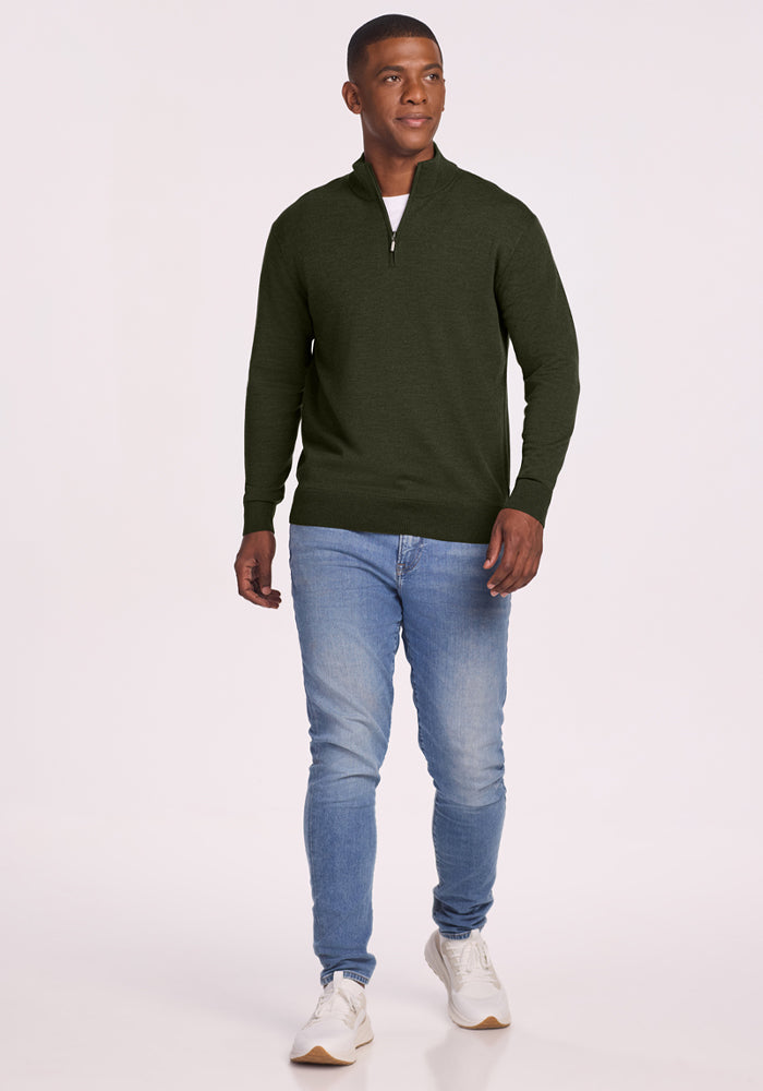 Man wearing Woolx Enzo Quarter Zip - Duffel Bag sweater, blue jeans, and white sneakers against a plain background.