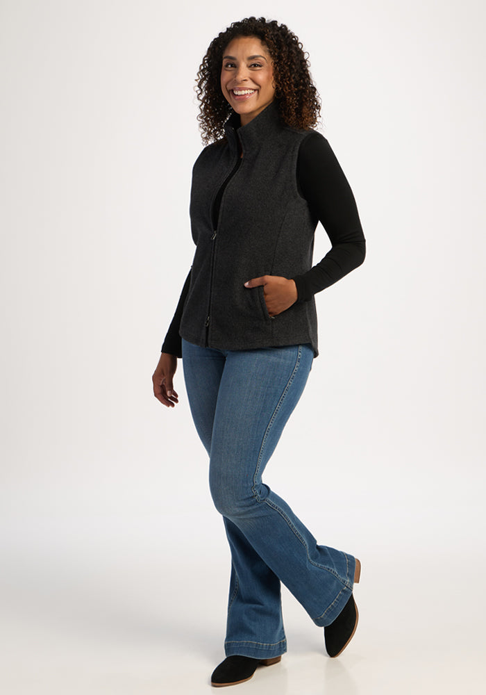 Woman wearing Woolx Haley Vest in Carbon Black, black top, and blue jeans, smiling on a white background.