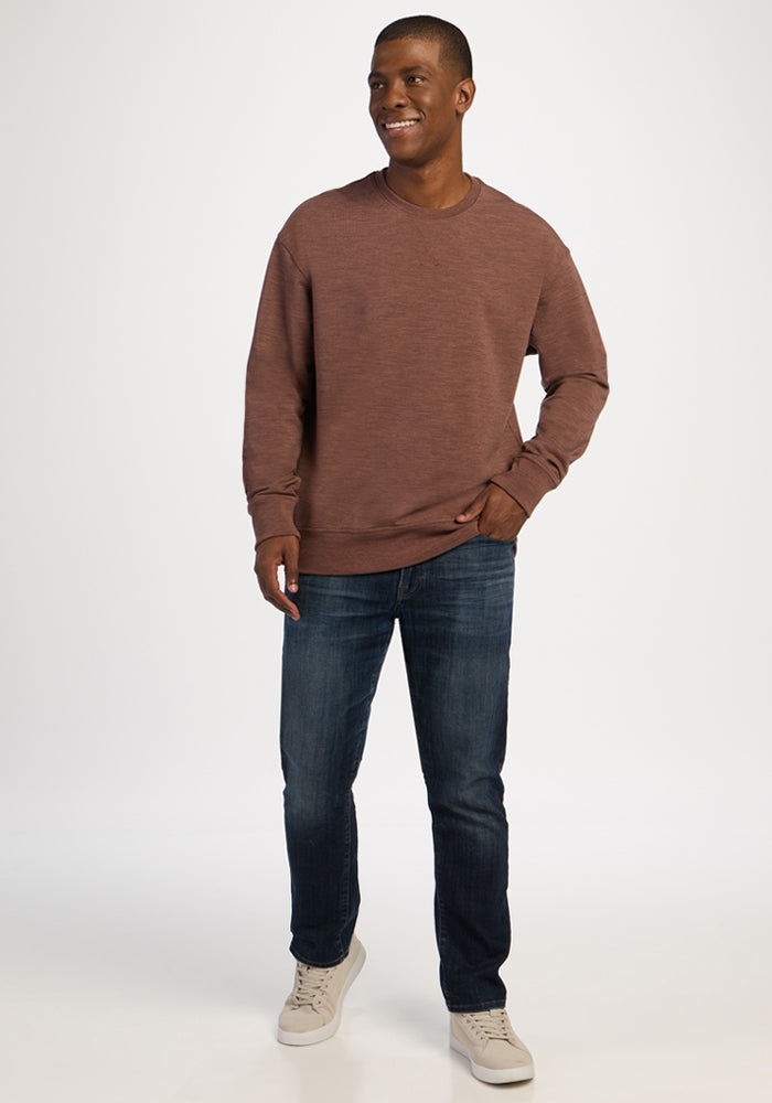 A man in a Sable Heather Woolx Miles Crewneck, dark blue jeans, and light-colored sneakers.