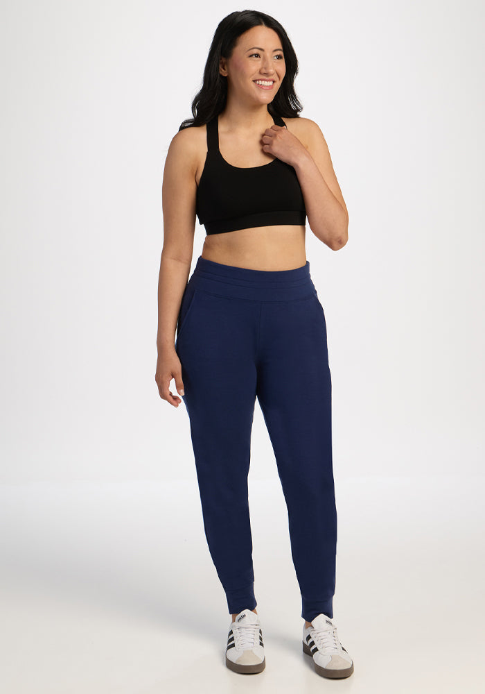 Woman models Woolx Willa Joggers - Ocean Cavern with a smile, one hand near her neck, against a white background.