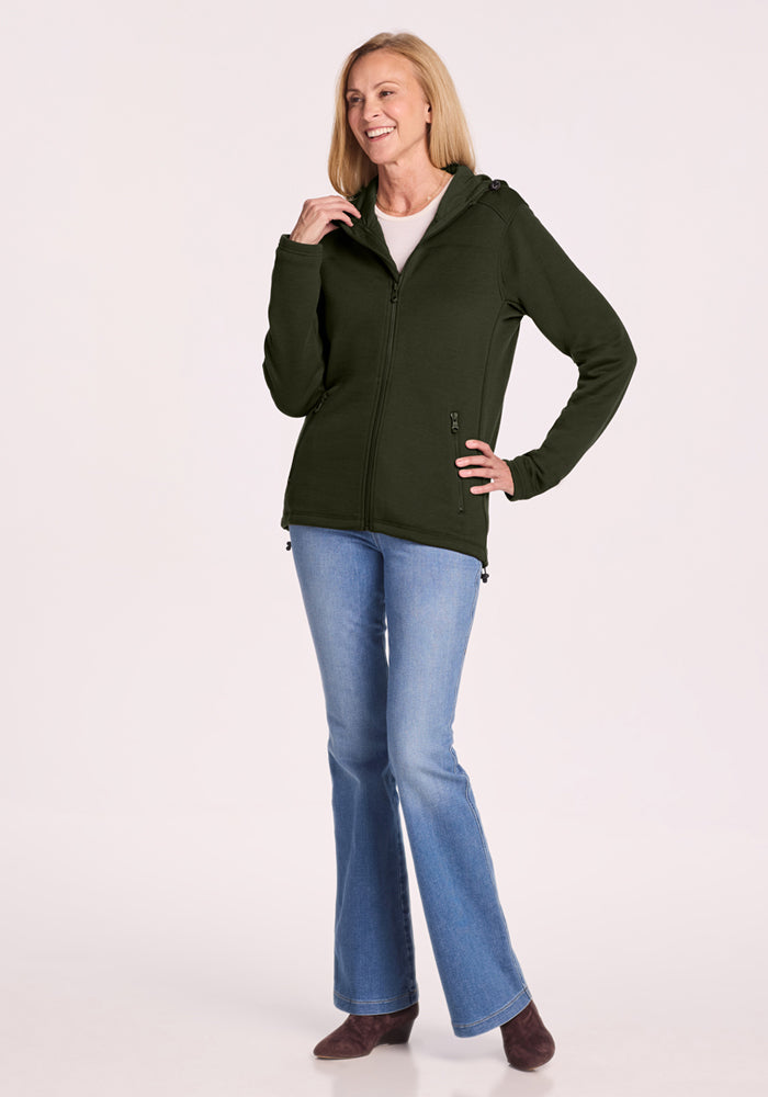 Woman standing and smiling, wearing a Woolx Cubby Hooded Sweatshirt - Duffel Bag, light blue jeans, and brown boots.