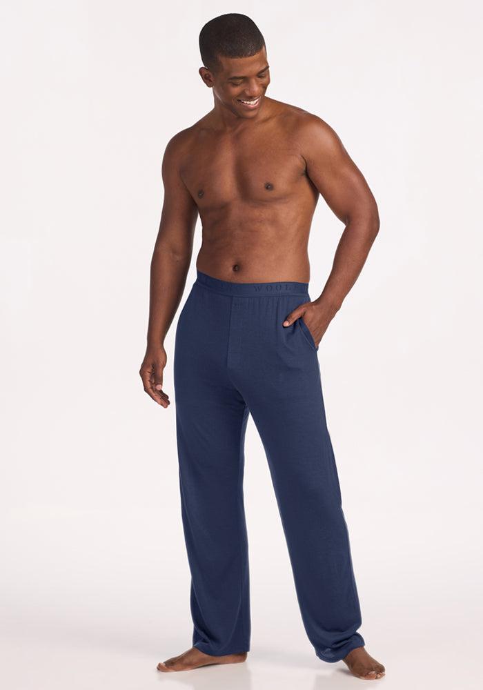 A shirtless man with his hand in the pocket of his dark blue Woolx Arlo Lounge Pants - Deep Dive.