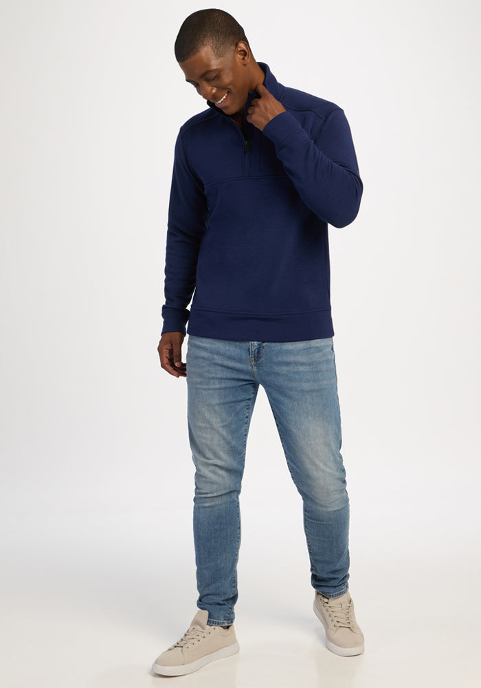 Smiling man in Woolx Mason 1/4 Zip - Ocean Cavern, light blue jeans, and beige sneakers against a white backdrop.