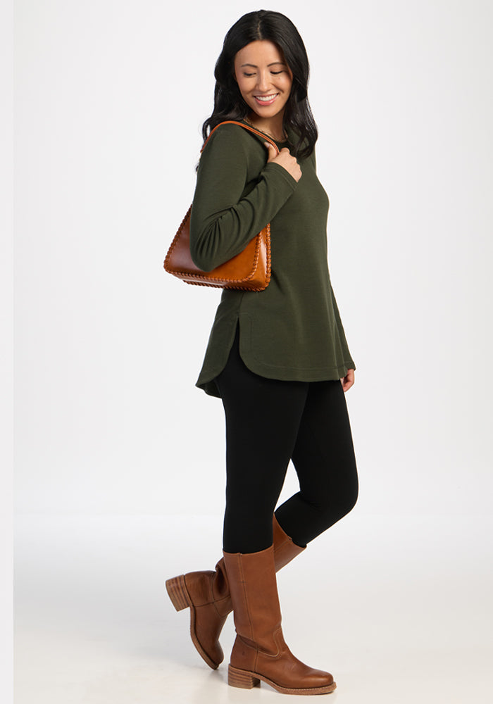 Woman in a Woolx Blair Tunic - Duffel Bag, black leggings, brown boots, and purse, smiling and looking down.