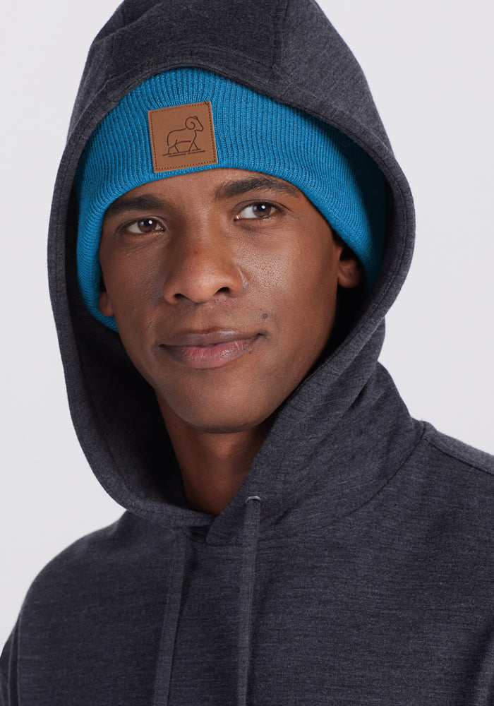 Man in a dark hoodie and Woolx Baylor Beanie - Blue Razz with brown patch, looking to the side against light background.
