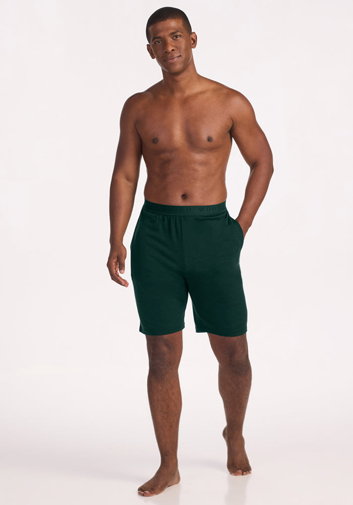 A shirtless man wearing deep pine Archer Lounge Shorts in Merino wool with pockets.