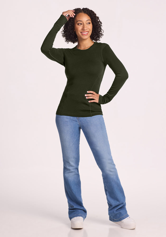 Woman wears Woolx Hannah Long Sleeve Top in Duffel Bag, smiling with one hand in curly hair and blue jeans.