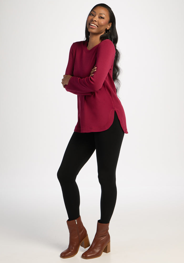 Woman wearing the Blair Petite Tunic in Beet Red by Woolx, with black leggings and brown boots, smiling.