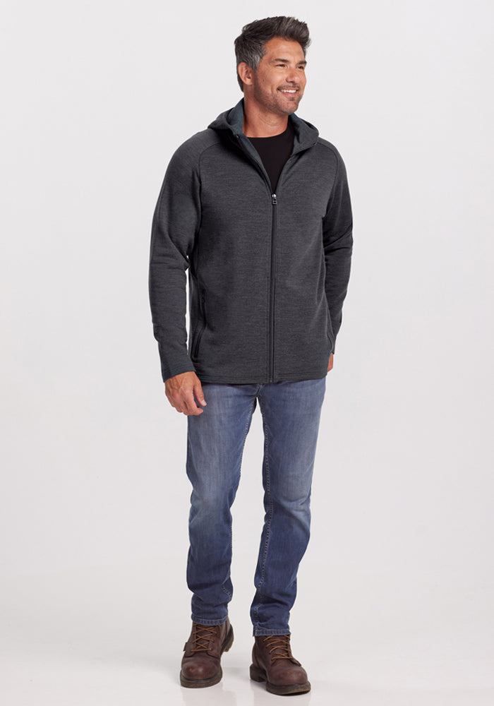 Smiling man in Woolx Boulder Hoodie - Cinder Melange, jeans, and brown boots stands against a plain white background.