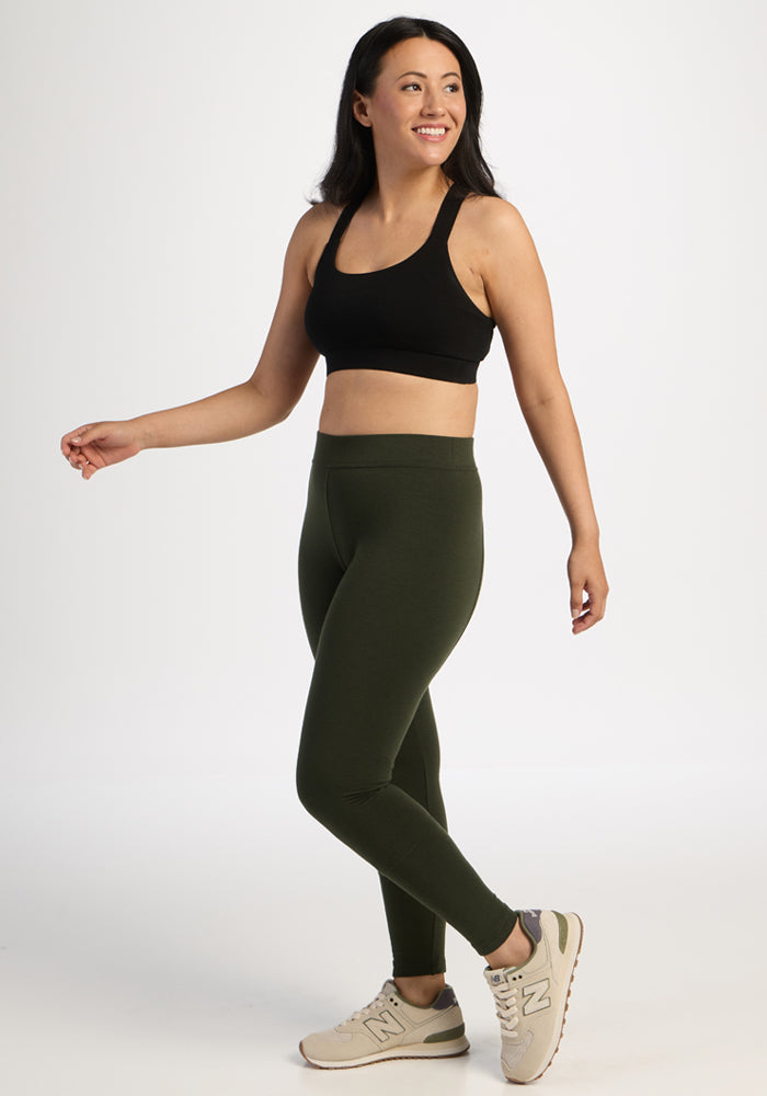 Woman in black sports bra, Woolx Stella Leggings - Duffel Bag, and beige sneakers smiles against a white background.