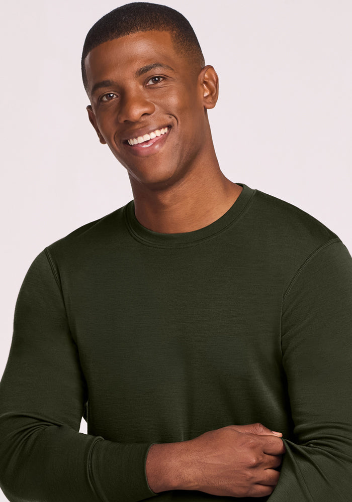 Smiling man wears the Woolx Explorer Base Layer - Duffel Bag, arms crossed, exuding comfort against a light backdrop.