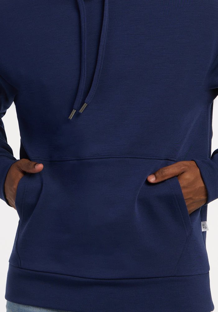 Model wears Woolx Watson Pullover - Ocean Cavern, hands in front pocket; only torso and hands are shown.