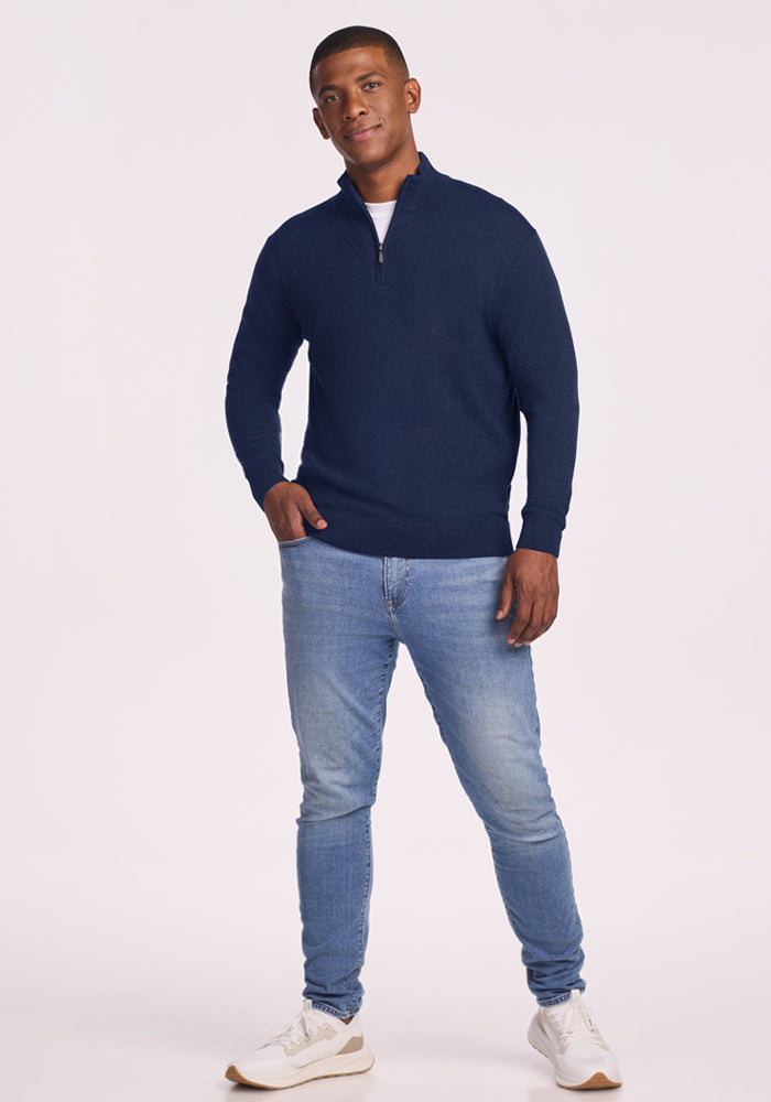 Man in Woolx Enzo Quarter Zip - Ocean Cavern, light blue jeans, and white sneakers stands against a plain background.