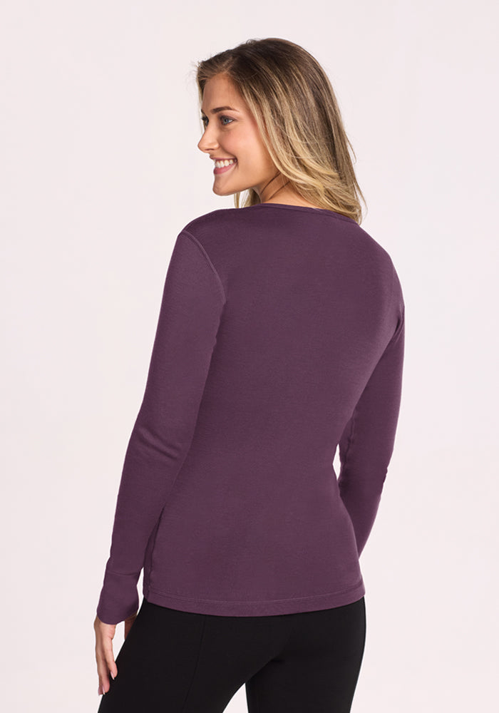 Woman smiling in a Woolx Hannah Long Sleeve Top - Purple Iris and black pants, back view, light background.