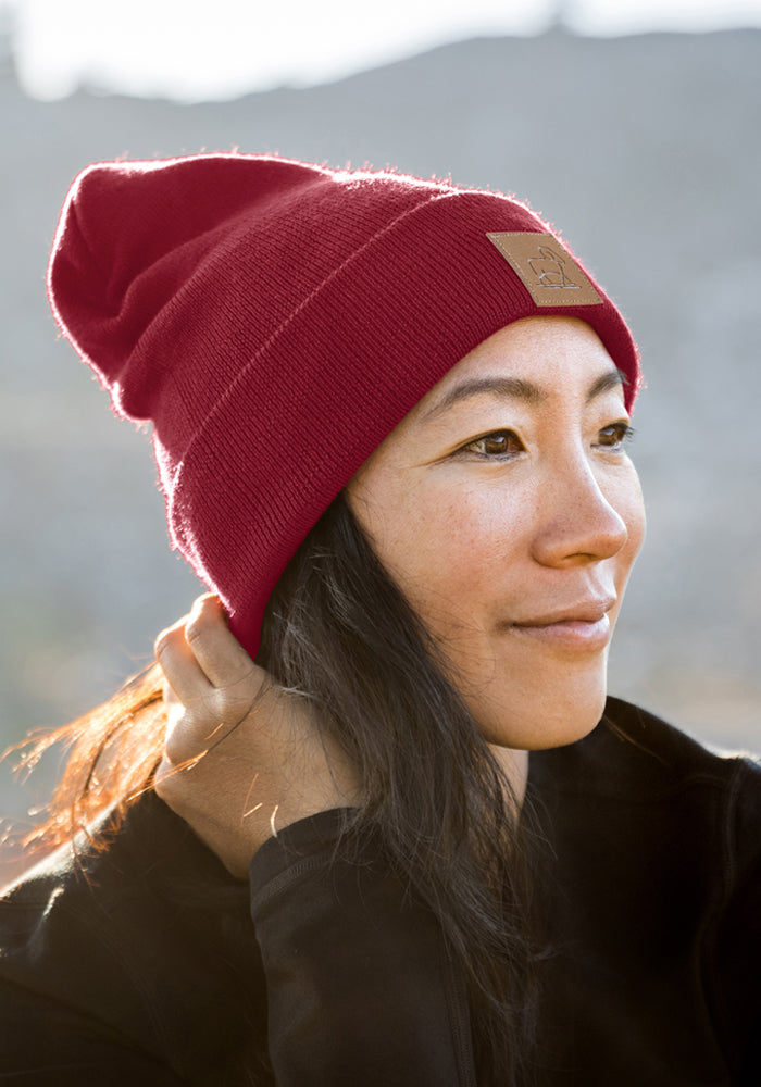 Woman in Woolx Baylor Beanie - Pinot Noir and black top, gazing sideways with a soft smile in natural light.