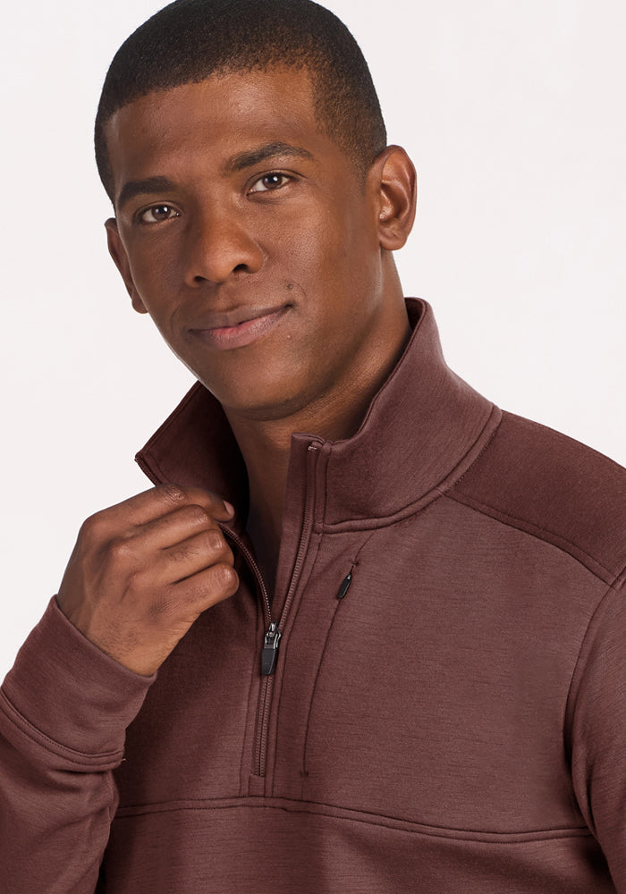 Man in Woolx Mason 1/4 Zip - Canyon Clay, gazing at camera with slight smile, hand on the zipper.