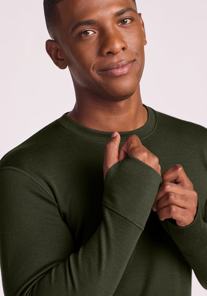 Man in Woolx Glacier Long Sleeve Crew - Duffel Bag looks at camera, hands by collar, wearing a slight smile.