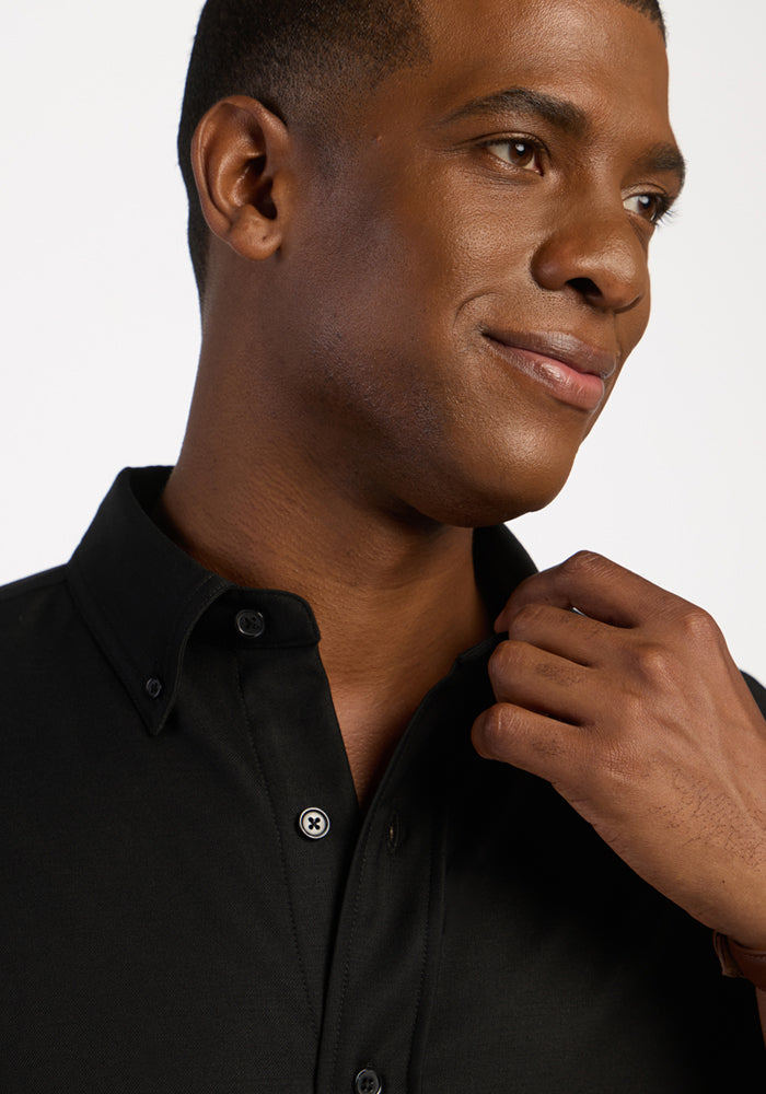 Man in a Woolx Nash Button Up - Black, smiling slightly, looking to the side, touching his collar.