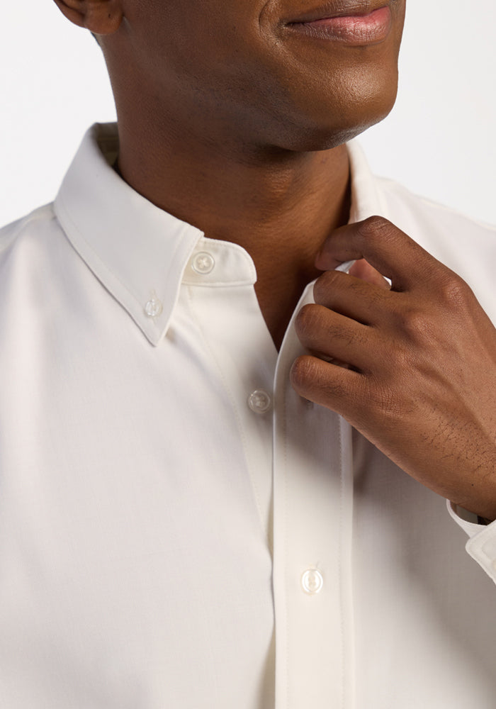A person adjusts the collar of a Woolx Nash Button Up - Eggshell, smiling slightly, shown from the shoulders up.