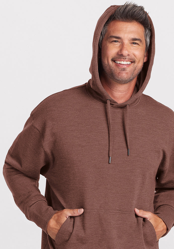 Smiling man in a Woolx Chase Hoodie - Sable Heather, hands in pocket, standing against a plain background.