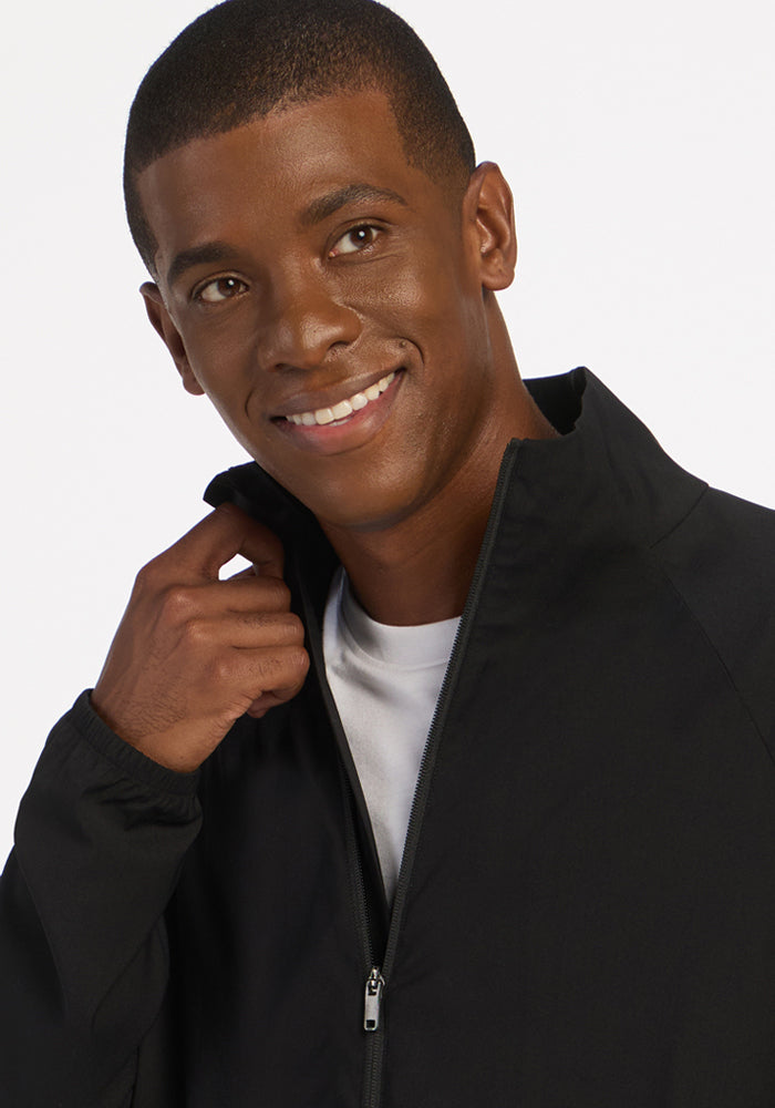 Man in Woolx Dominator Windbreaker—black, lightweight jacket over white shirt, touching collar, white background.