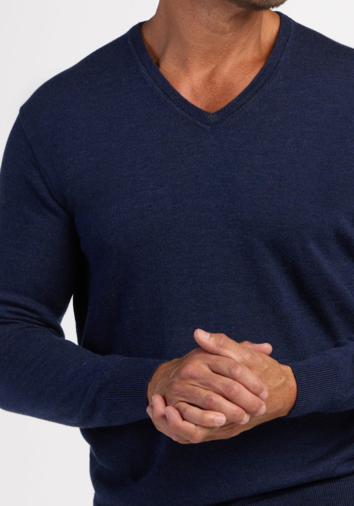 Man in a Woolx Vincenzo Sweater - Ocean Cavern, clasping hands—a men’s wardrobe staple against a white background.