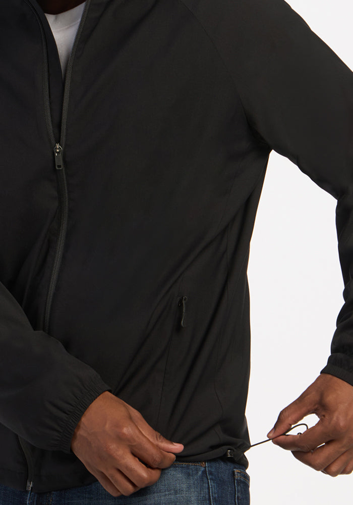 A person tightens the drawcord on a Woolx Dominator Windbreaker - Black while wearing blue jeans.