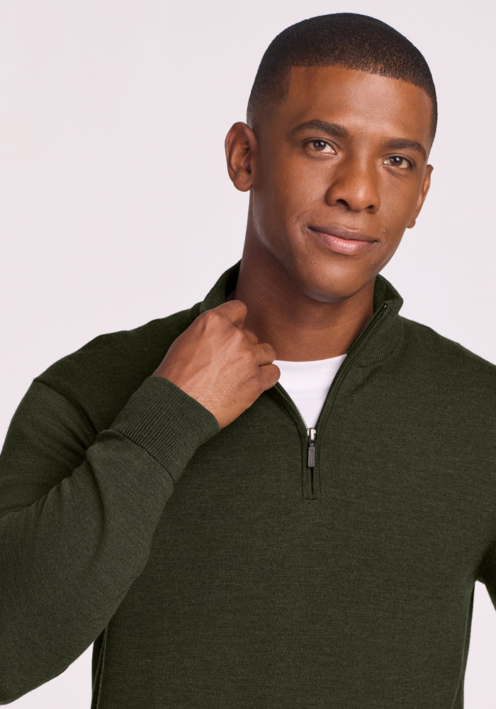 Man in a Woolx Enzo Quarter Zip - Duffel Bag sweater, holding the collar and smiling softly against a plain backdrop.
