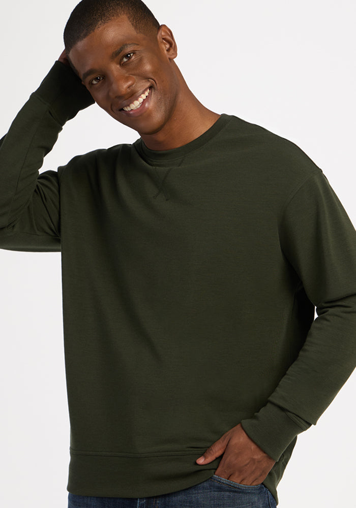 Smiling man wearing a moisture-wicking, long-sleeved dark green heavyweight merino Miles Crewneck - Duffel Bag.