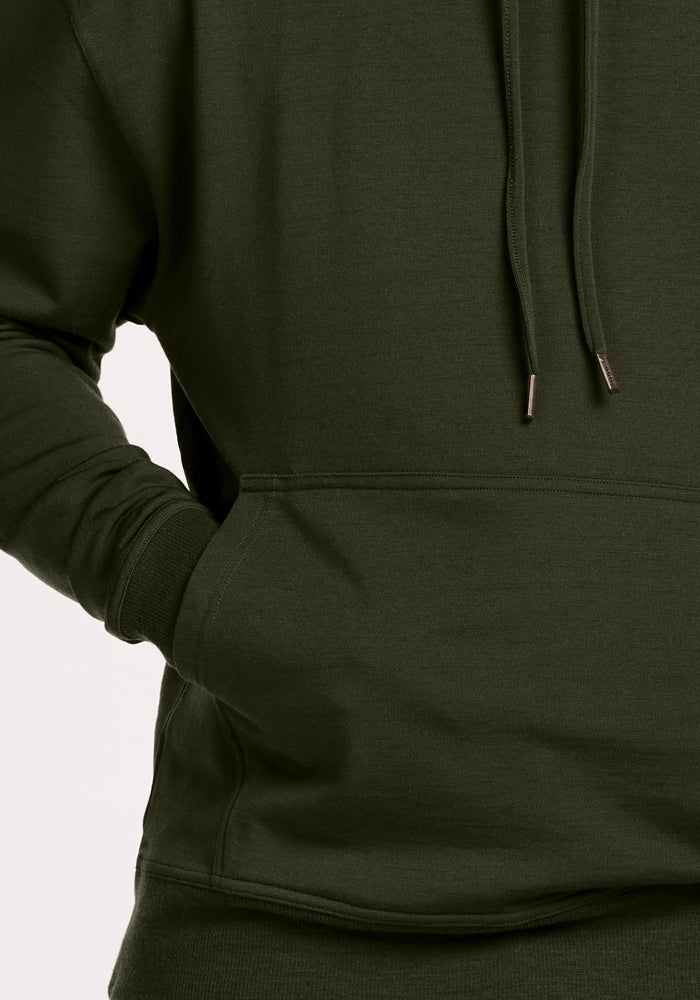 Someone wears the Woolx Chase Hoodie - Duffel Bag in dark green, one hand casually tucked into its front pocket.