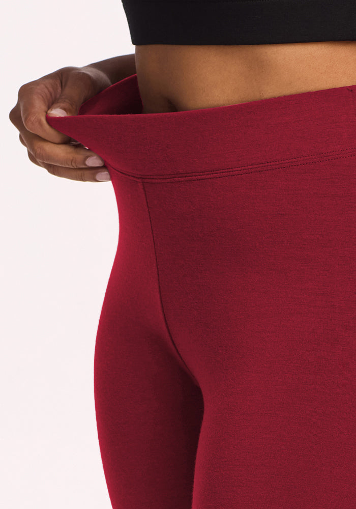 A person pulls at the waistband of Woolx Stella Leggings - Pinot Noir, showing their flattering fit and stretchy fabric.