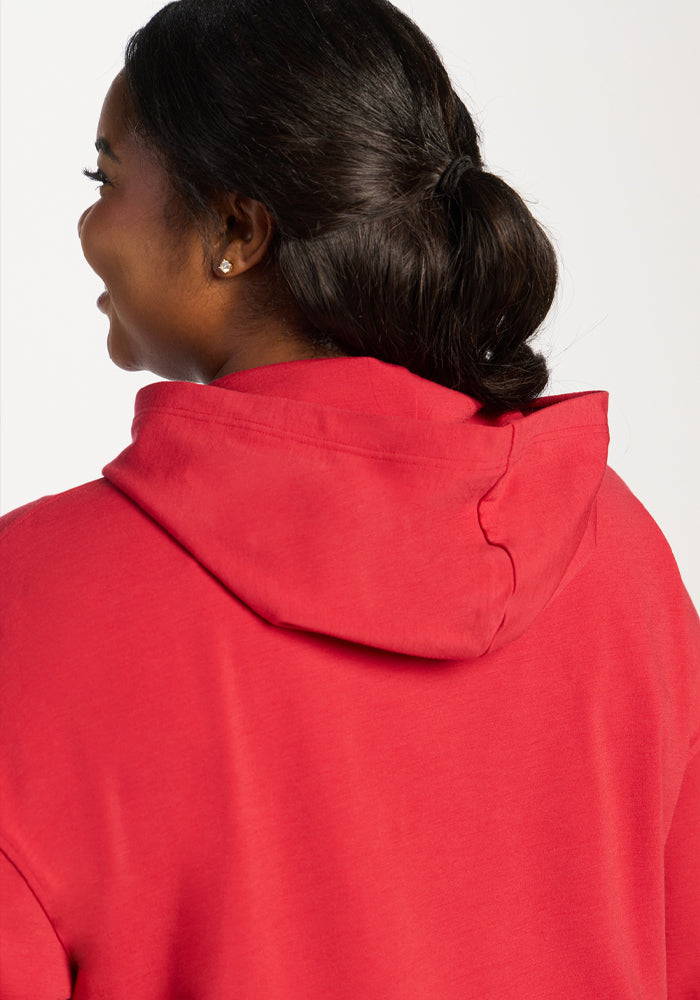 Woman with dark hair in a low bun wears the Woolx Lizzy Hoodie in Maraschino Cherry, shown from behind and smiling.