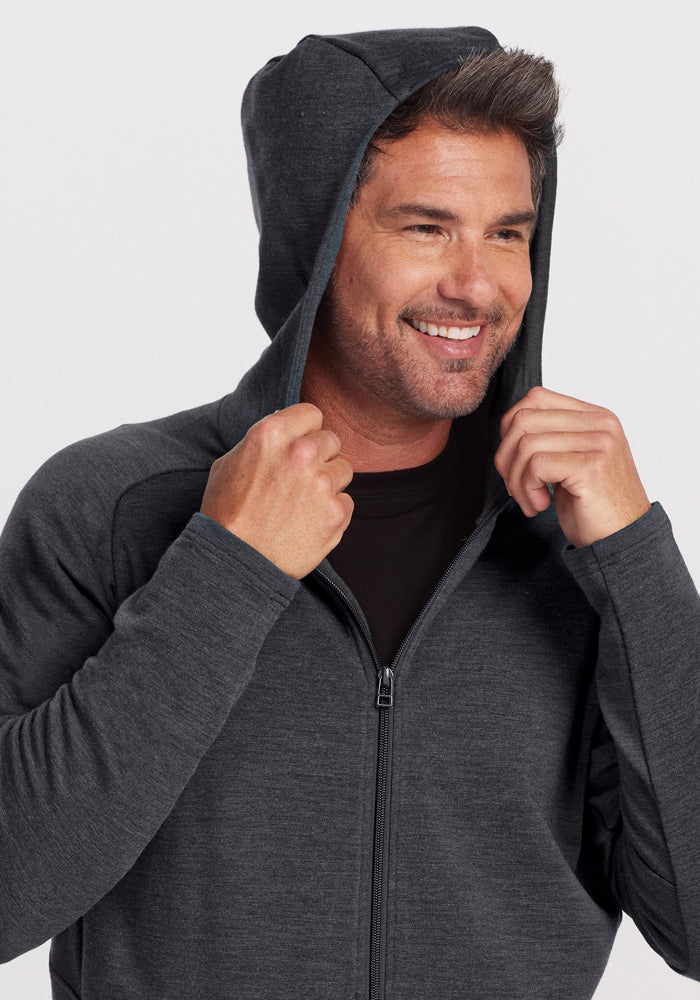Smiling man in Woolx Boulder Hoodie - Cinder Melange holds hood near face against a plain white background.