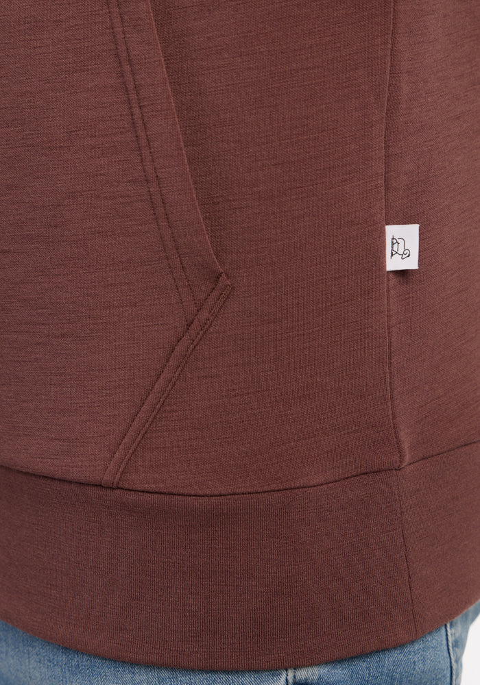 Close-up of a Woolx Watson Pullover - Canyon Clay pocket, showing a small white tag and blue jeans at the bottom.