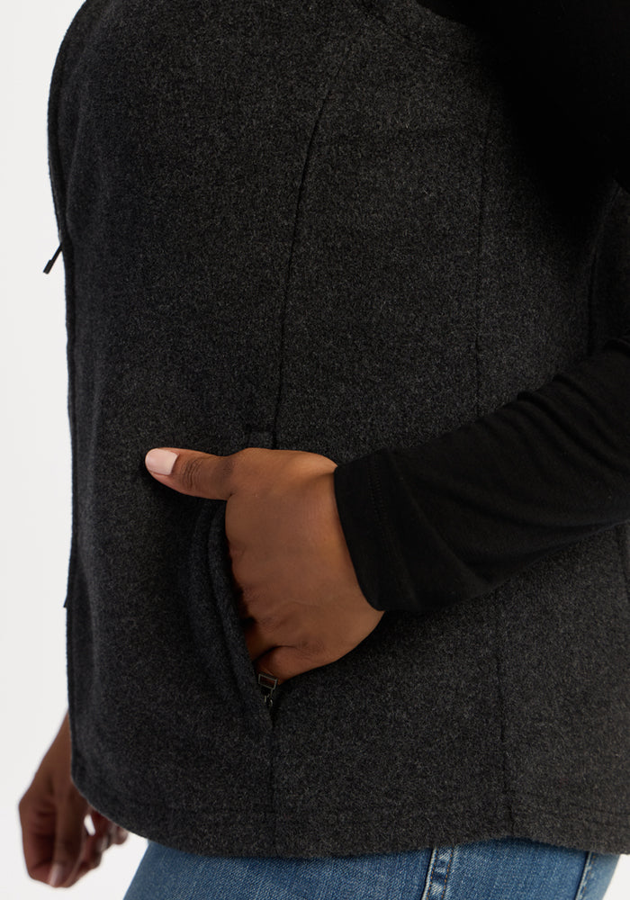 A person wears the Woolx Haley Vest - Carbon Black with jeans, hand in pocket; only their torso and arm are visible.