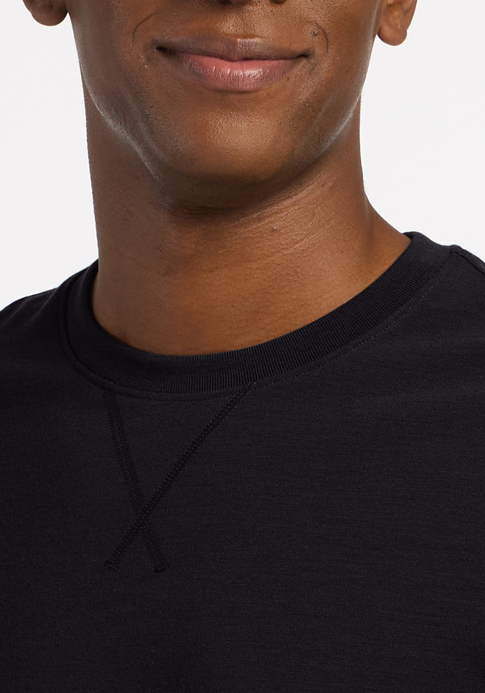 A person wearing a black Woolx Miles Crewneck in heavyweight merino wool with a v-stitch detail at the collar.
