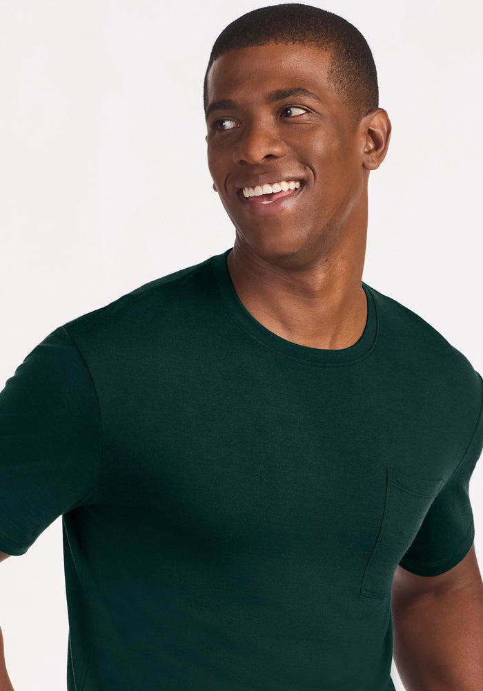 A man smiles wearing a dark green Woolx Finn Top - Deep Pine, an odor-resistant crew-neck t-shirt with a chest pocket.