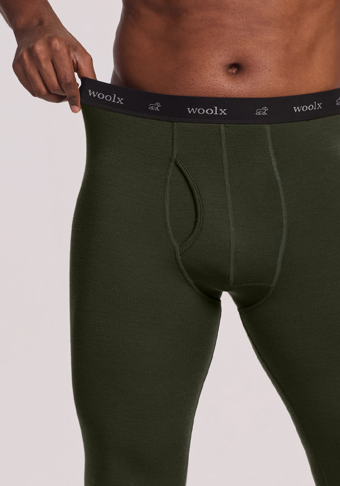 Man wears Woolx Arctic Leggings - Duffel Bag, pulling waistband to show stretch and Merino wool base layer fit.