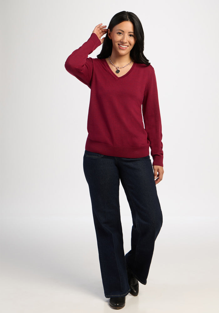 Woman in a Woolx Francesca Sweater - Beet Red and dark jeans smiles, raising one hand to her head.
