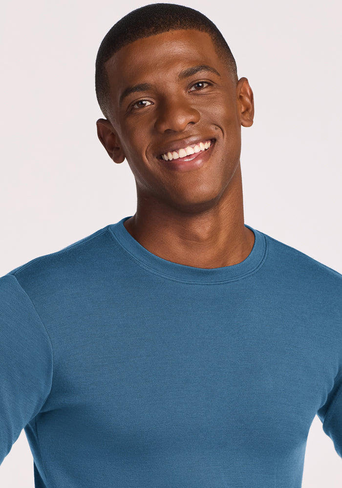Smiling man in a Woolx Easton Crew Neck Shirt - Blue Ashes stands against a plain light background.