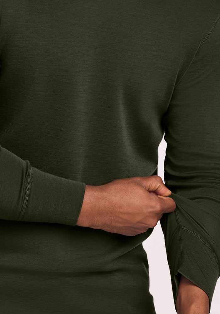 A person in a dark green Woolx Explorer Base Layer - Duffel Bag pulls up a sleeve, showing moisture-wicking fabric.