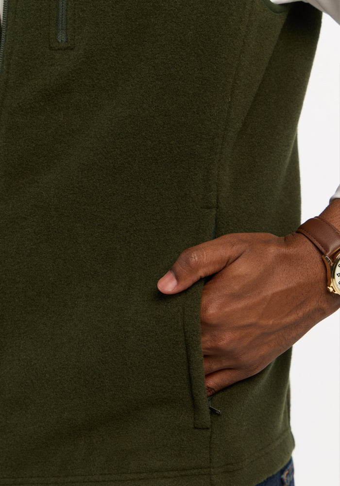 A hand in the zippered pocket of an olive green Woolx Everest Vest - Duffel Bag.